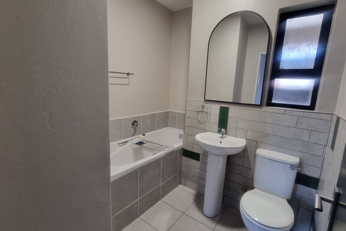 A clean, modern bathroom featuring a pedestal basin, built-in bathtub, toilet, and neutral tiled finishes with a frosted window for privacy.