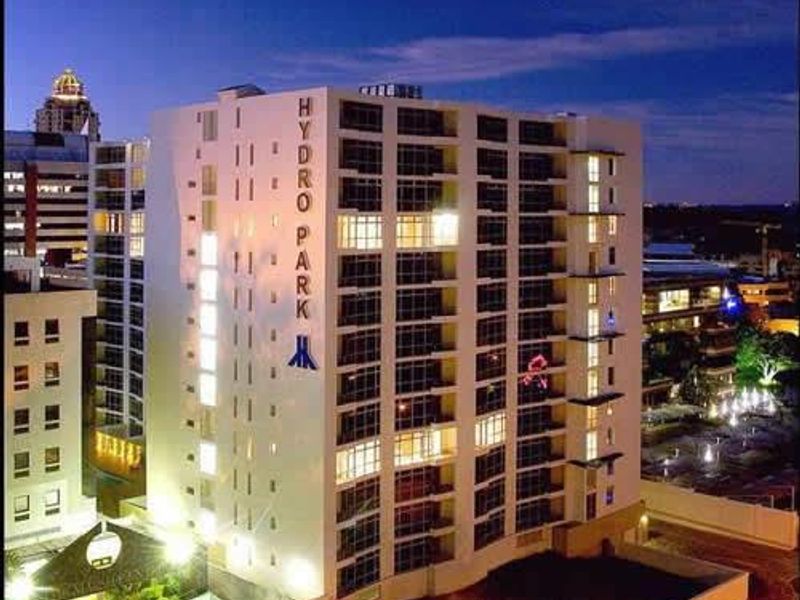 A night-time aerial view of the Hydro Park apartment building, showcasing its multi-story facade, glass windows, and surrounding landscaped grounds.