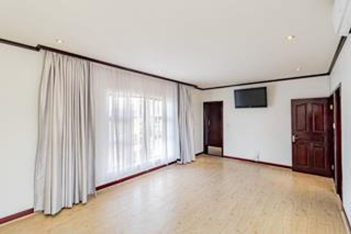 A spacious, empty bedroom featuring light-toned laminate flooring, recessed downlighting, and neutral walls, ready for personalization.