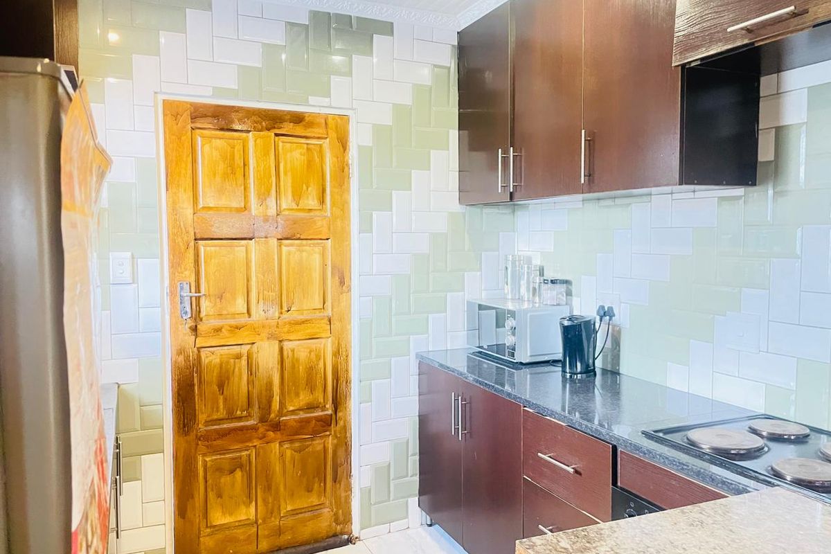 A functional kitchen featuring dark wood cabinetry, granite-style countertops, a built-in electric hob, and a distinctive two-tone tiled wall finish.