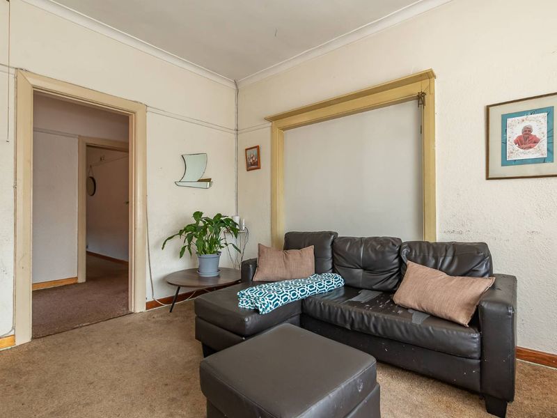 A living room featuring original architectural details including cove cornicing and timber architraves, requiring cosmetic updates to the wall finishes and flooring.