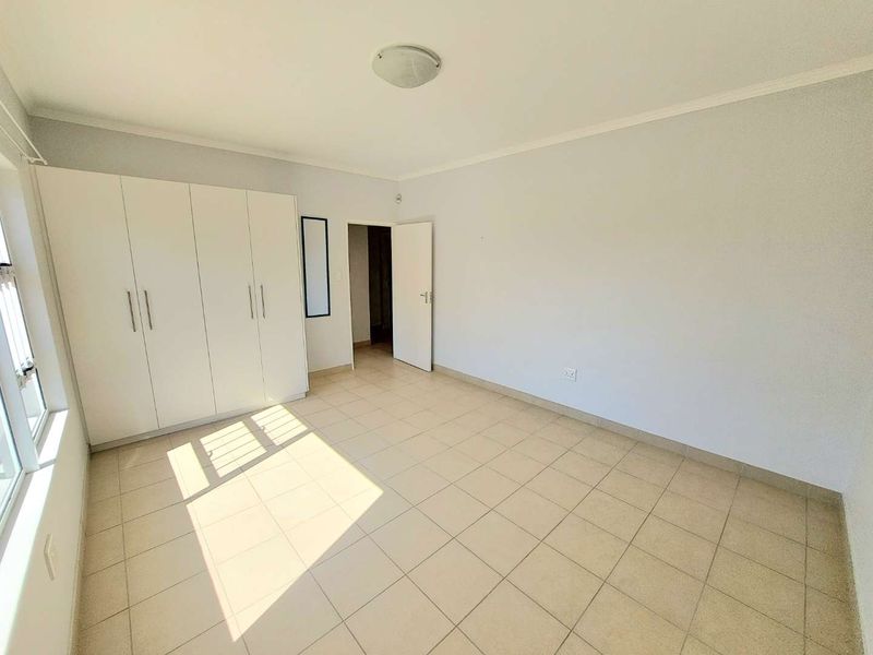 A bright, empty bedroom featuring neutral tiled flooring and ample built-in cupboard storage space.