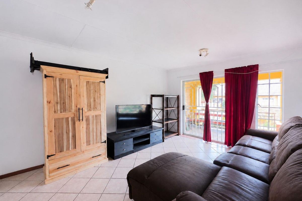 A living room featuring tiled flooring and a sliding glass door with security gate, providing access to an outdoor balcony area.