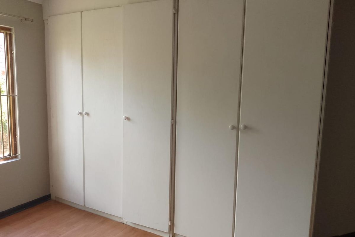 A bedroom featuring built-in white cabinetry and wood-look flooring, providing ample storage space and natural light from the side window.