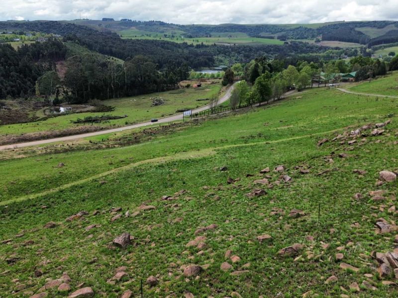 A wide-angle view of the vacant residential land, showcasing the rolling green landscape, natural rock formations, and surrounding rural scenery.