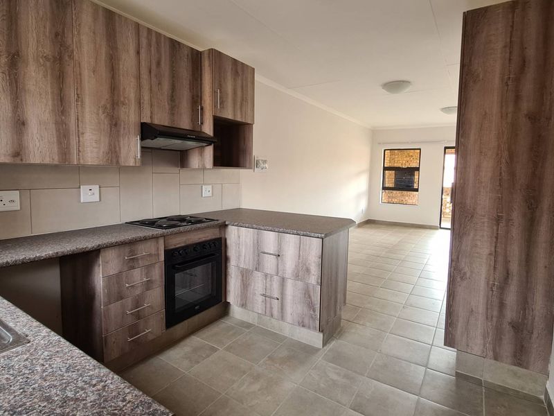 Open-plan kitchen featuring modern wood-look cabinetry, stone-effect countertops, and integrated appliances, flowing into a spacious living area with tiled floors.