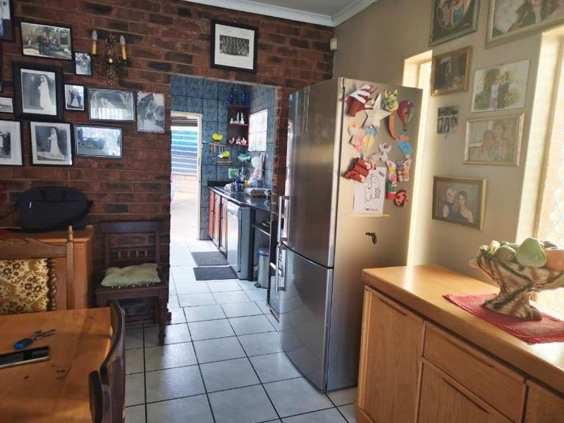 A kitchen area featuring exposed brick walls, tiled flooring, and built-in cabinetry, with a view leading into a secondary prep or scullery space.