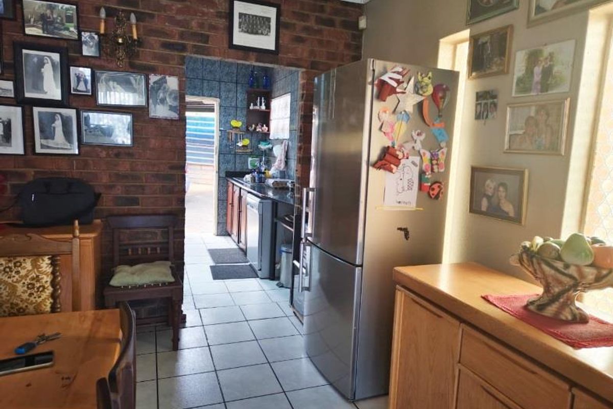 A kitchen area featuring exposed brick walls, tiled flooring, and built-in cabinetry, with a view leading into a secondary prep or scullery space.