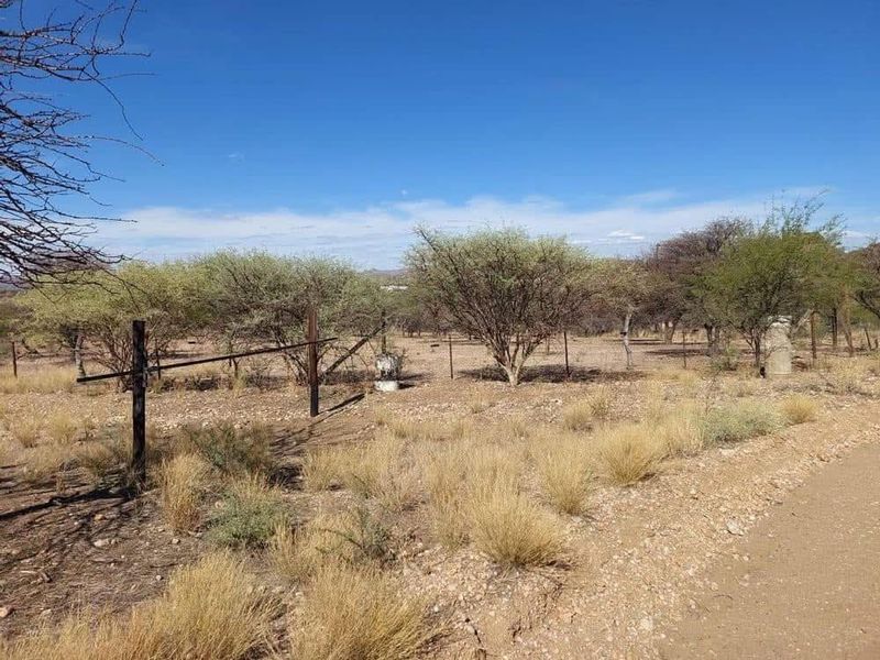 A view of a vacant residential plot featuring natural vegetation, dry grass, and existing wire perimeter fencing along an unpaved access road.