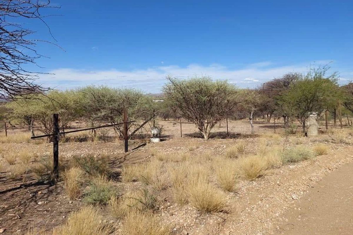 A view of a vacant residential plot featuring natural vegetation, dry grass, and existing wire perimeter fencing along an unpaved access road.