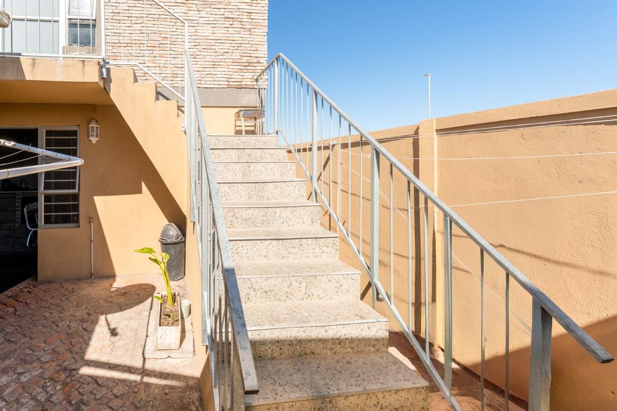 Exterior staircase with metal railings leading to an upper level, featuring stone-tiled steps and a paved courtyard area.