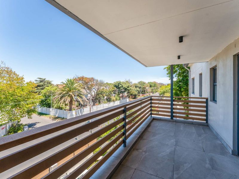 A clean, modern balcony featuring tiled flooring, horizontal slat railings, and recessed ceiling lighting, offering an open view of the surrounding neighborhood.