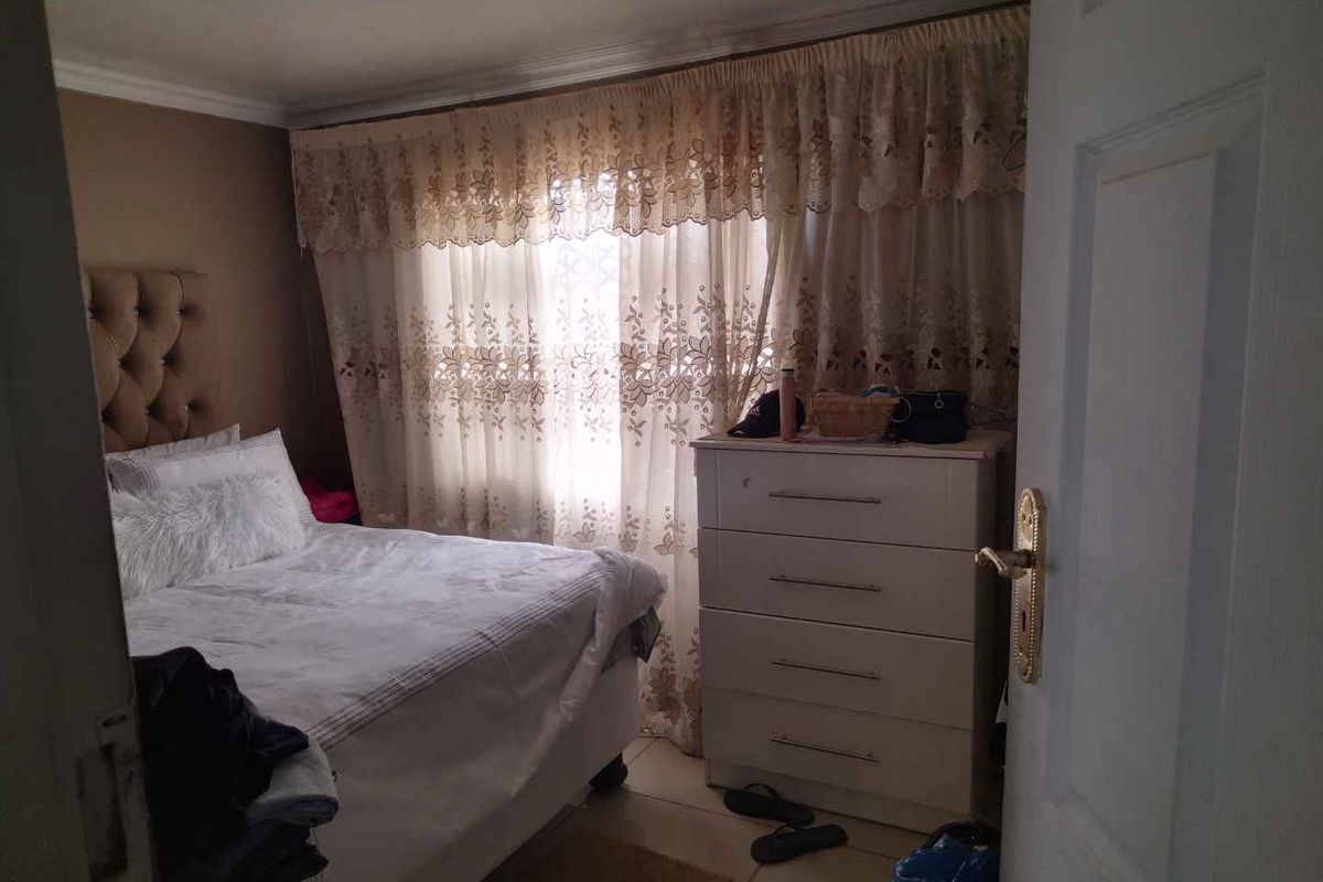 A bedroom featuring tiled flooring and a window with curtain treatments, viewed from the doorway.