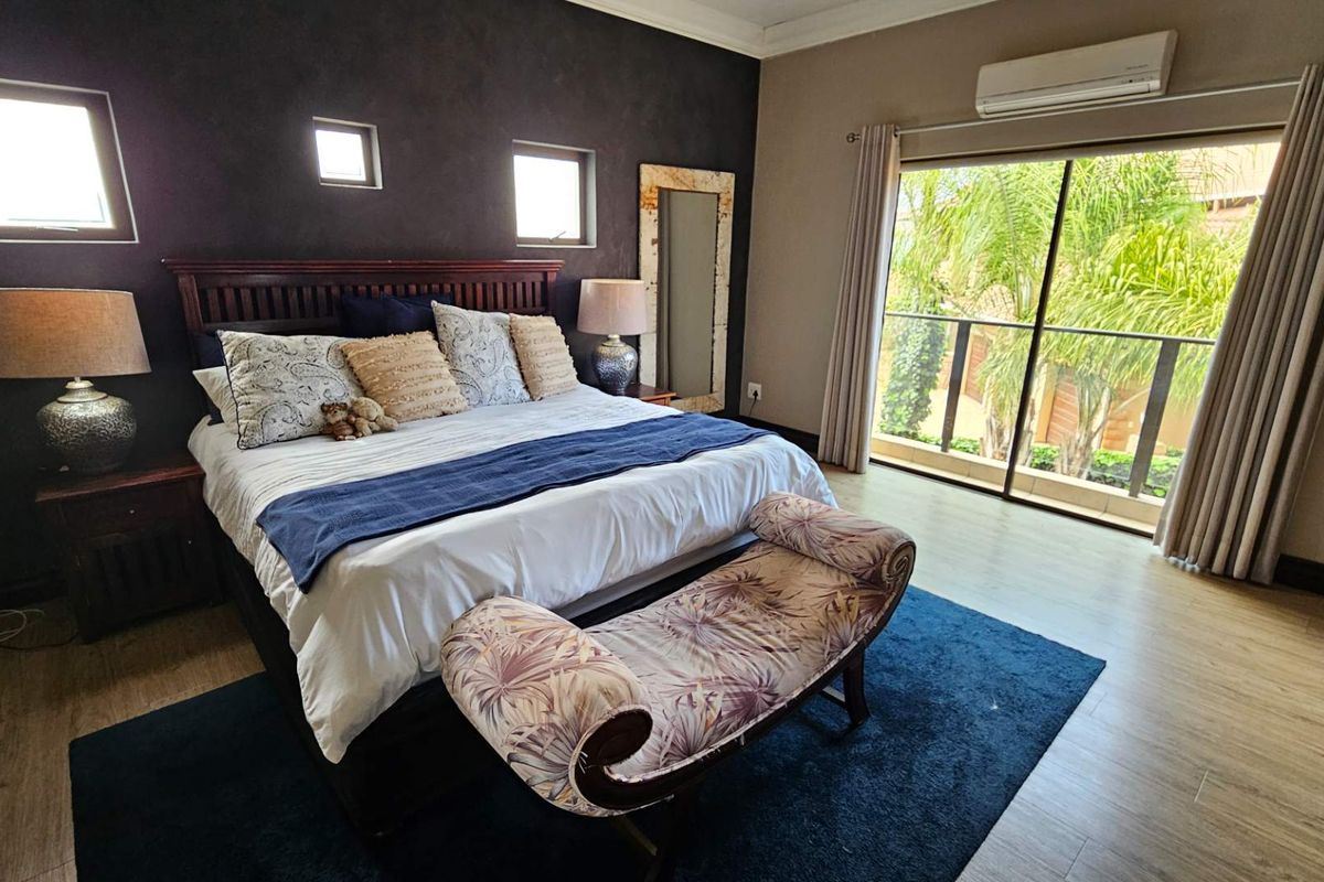 Spacious bedroom featuring laminate flooring, a split-system air conditioner, and large sliding glass doors providing access to an outdoor balcony area.