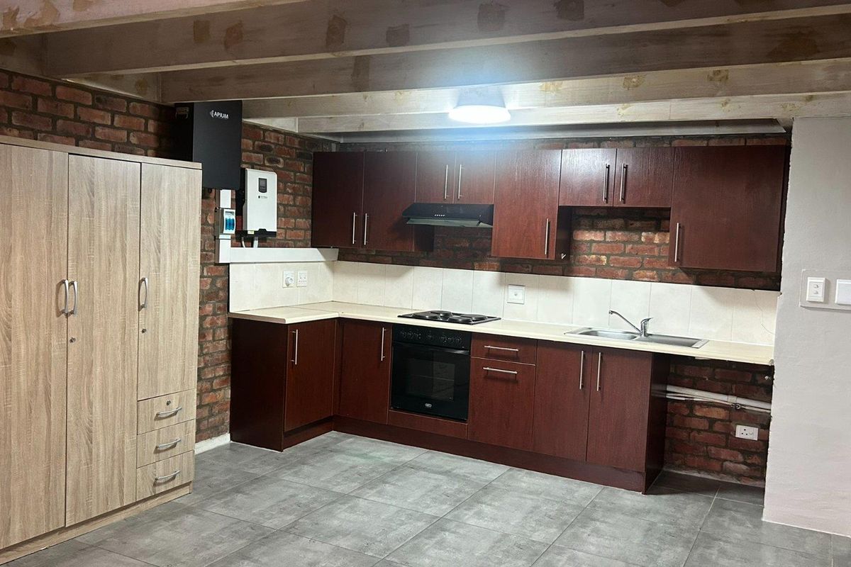 Kitchen featuring dark wood cabinetry, built-in oven and hob, exposed brick walls, and timber ceiling beams, providing a rustic industrial aesthetic.