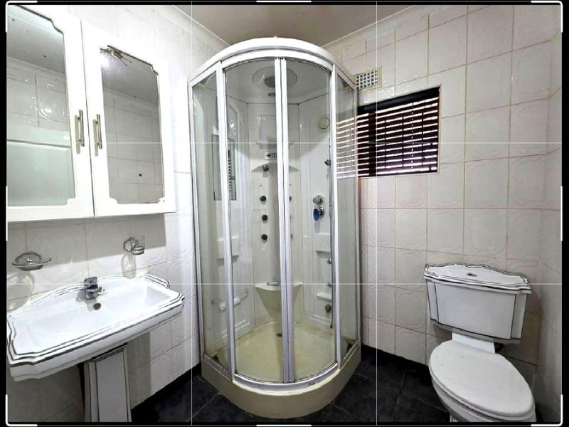 A functional bathroom featuring a pedestal basin, enclosed shower cubicle, and toilet, finished with tiled walls and flooring.