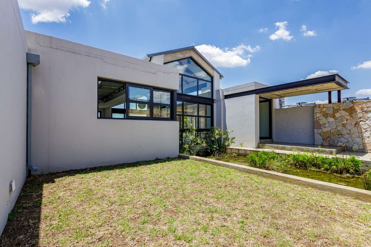 Modern architectural rear elevation featuring large glass windows, a covered walkway, and a landscaped garden with a water feature.