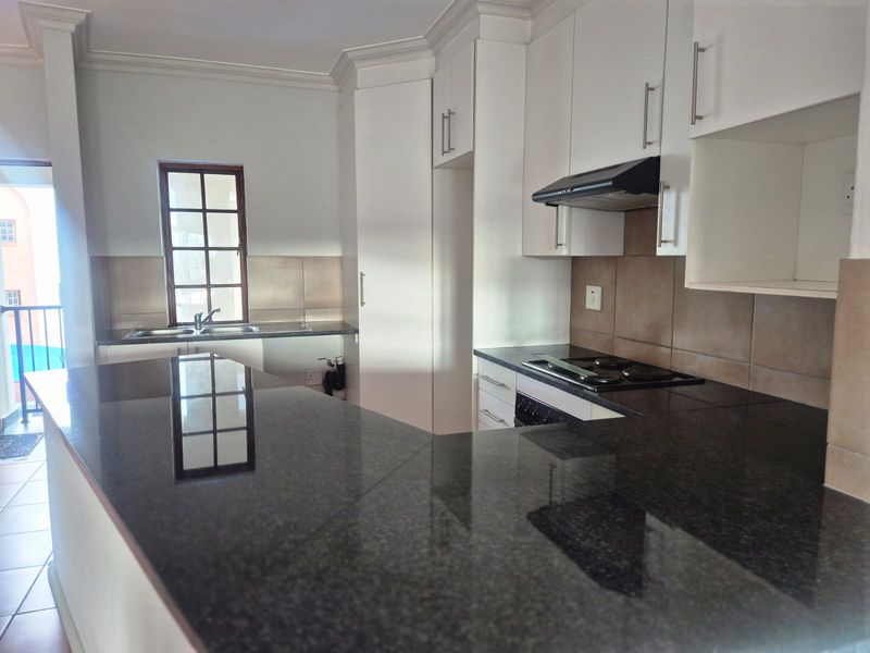 A clean, functional kitchen featuring dark granite countertops, white cabinetry, built-in oven and hob, and a tiled backsplash with a window for natural light.