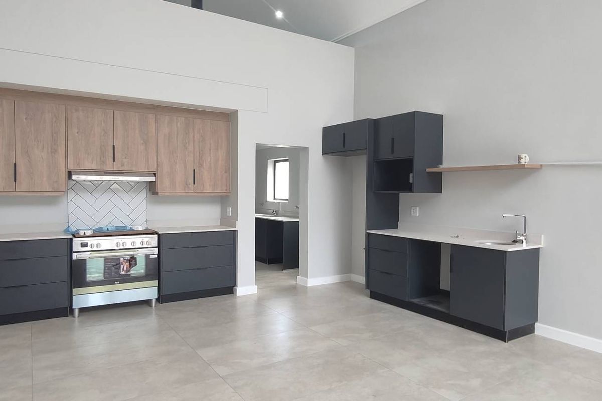 Modern kitchen featuring two-tone cabinetry, stone countertops, a herringbone tile backsplash, and a stainless steel freestanding oven with an integrated extractor fan.