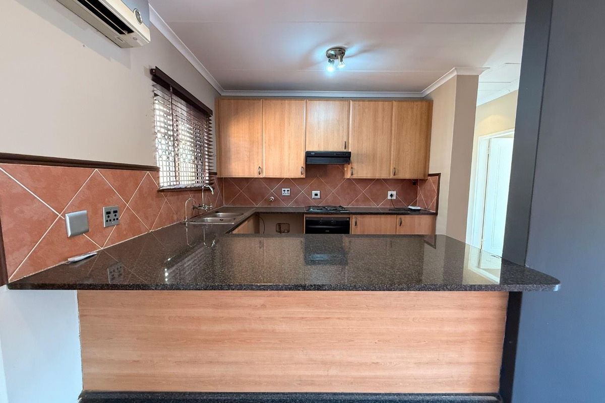 A functional kitchen featuring granite countertops, wooden cabinetry, built-in oven, hob, and extractor fan, with a breakfast bar overlooking the living area.