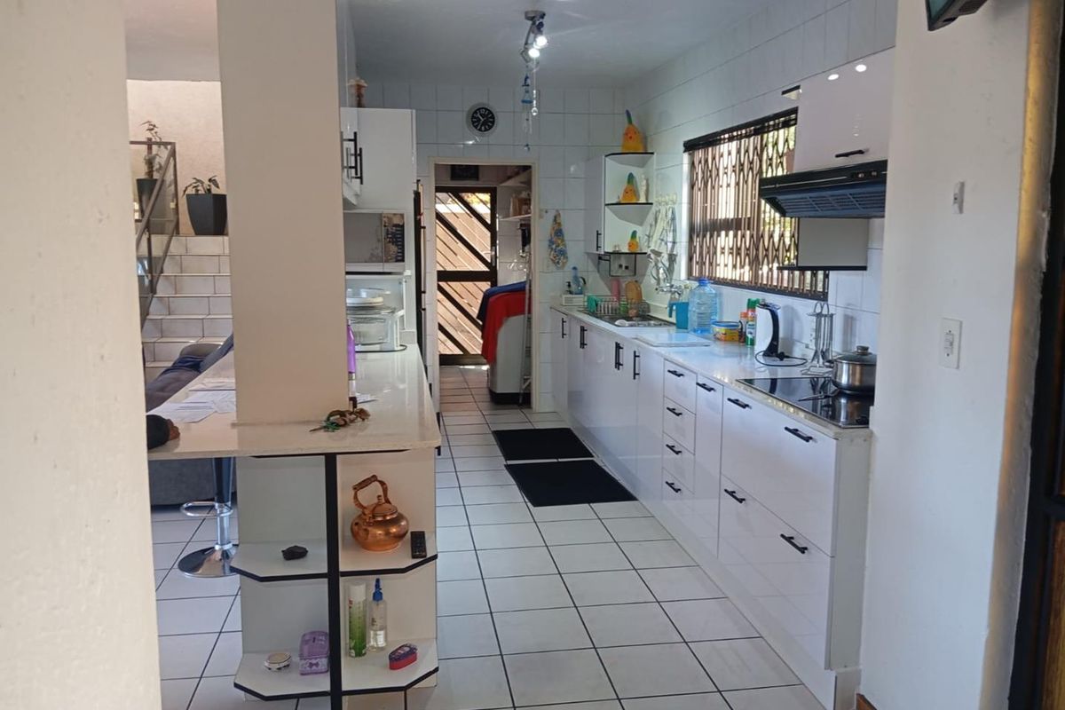 A functional kitchen featuring white cabinetry, integrated hob, extractor fan, and tiled flooring, with an adjacent breakfast counter and access to a utility area.