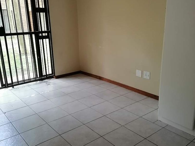 An empty living area featuring neutral tiled flooring, beige walls, and a secure sliding door with an integrated security gate.