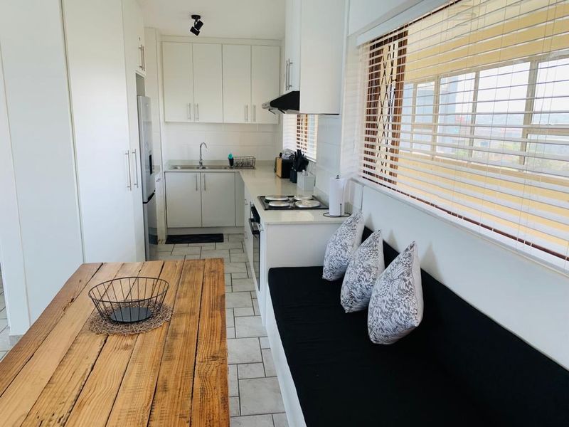 A functional kitchen featuring white cabinetry, integrated appliances including an oven and hob, tiled flooring, and a built-in bench seating area by the window.