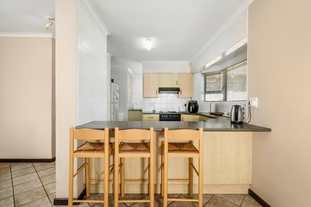 A functional kitchen featuring a breakfast bar, laminate cabinetry, tiled splashbacks, and a built-in cooktop with an extractor fan.
