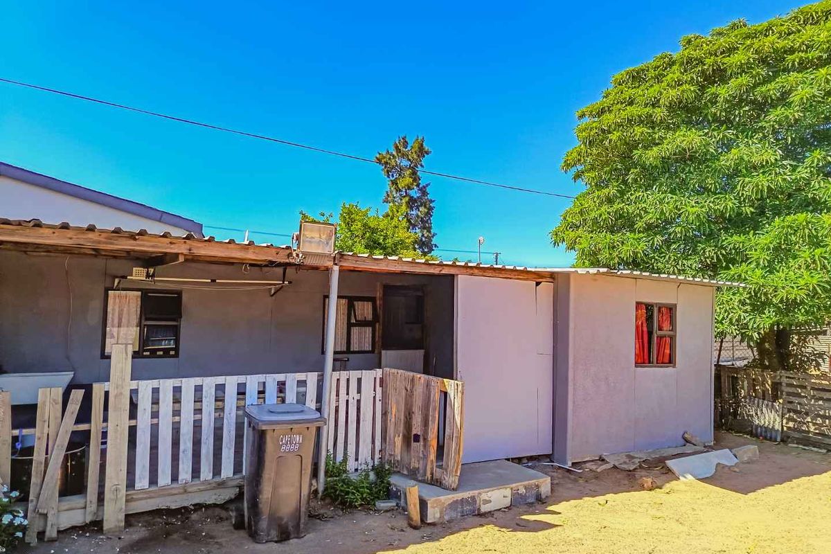Rear exterior view of the property featuring a covered patio area, basic wall finishes, and a surrounding yard space.