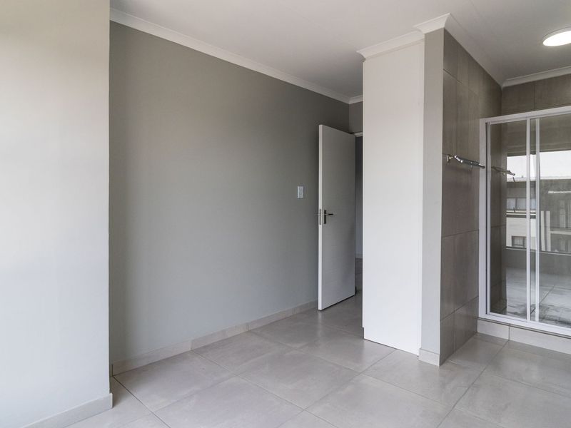 A clean, modern bathroom featuring a pedestal sink, a glass-enclosed shower, and neutral floor-to-ceiling tiling.