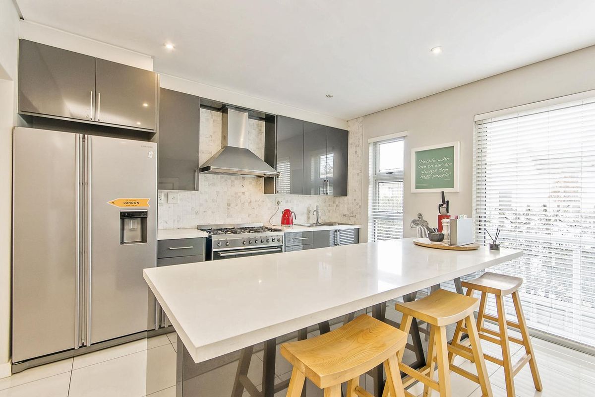 Modern kitchen featuring sleek grey cabinetry, a central island with a stone countertop, stainless steel gas stove, and tiled backsplash.