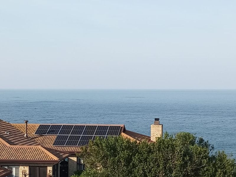A scenic elevated view overlooking the ocean, featuring a residential roof with installed solar panels and a brick chimney.