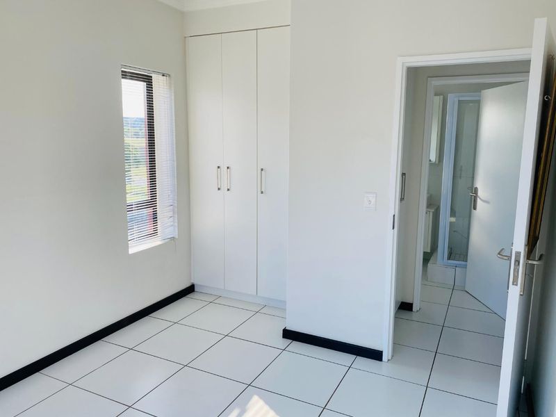A clean, empty bedroom featuring white built-in cupboards, tiled flooring, and an en-suite bathroom entrance.