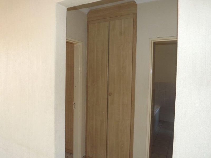 A functional hallway featuring built-in wooden cupboards and tiled flooring, providing access to adjacent rooms.
