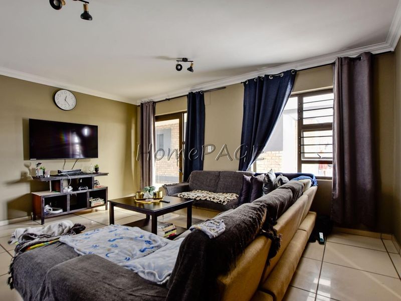 A comfortable living room featuring tiled flooring, aluminium window frames, and a sliding door leading to the exterior.