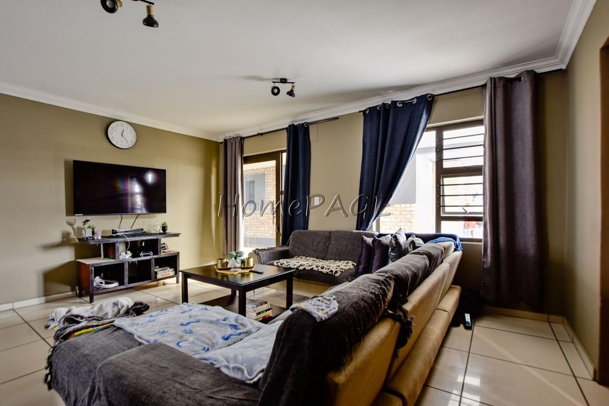 A comfortable living room featuring tiled flooring, aluminium window frames, and a sliding door leading to the exterior.