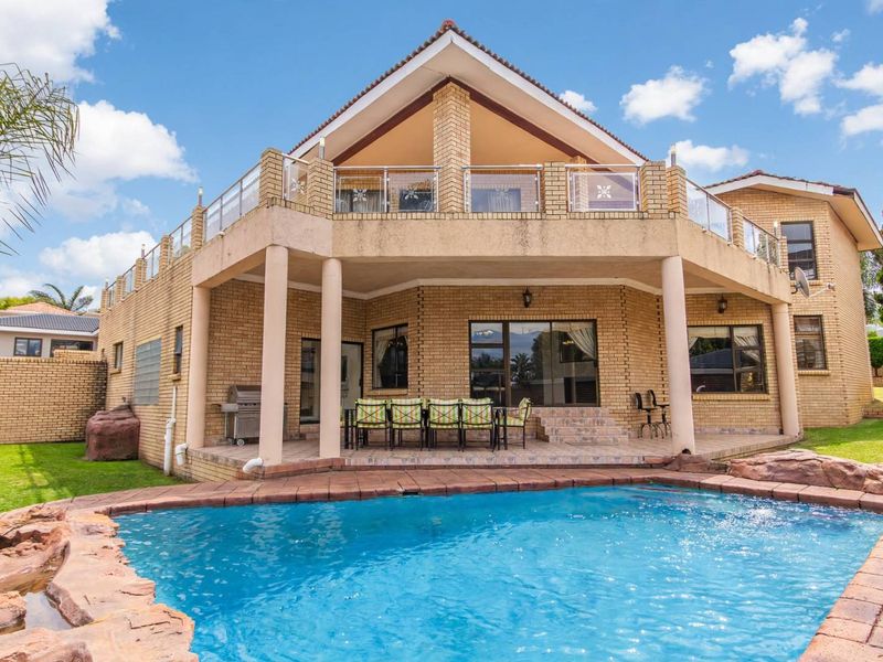 Rear view of a multi-level brick house featuring a swimming pool, covered patio area, and an upper-level balcony with glass balustrades.