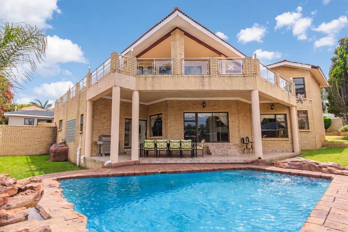 Rear view of a multi-level brick house featuring a swimming pool, covered patio area, and an upper-level balcony with glass balustrades.