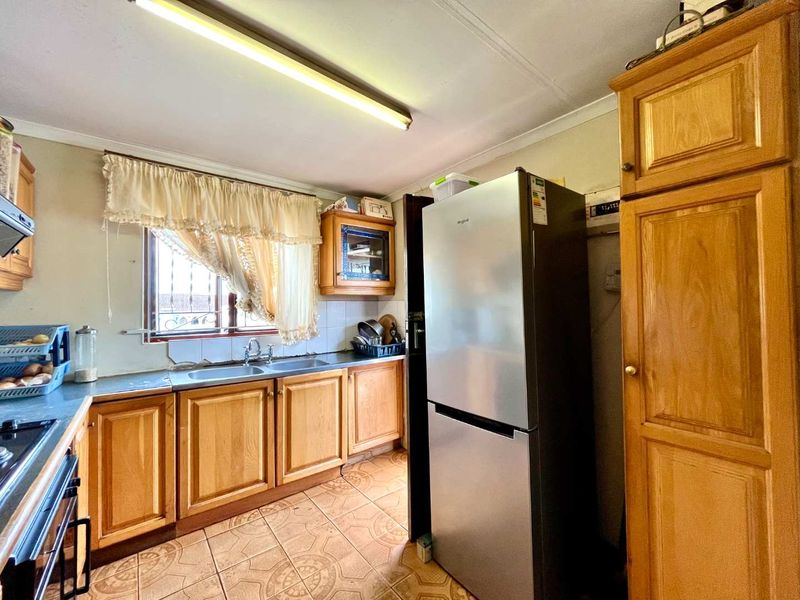 A functional kitchen featuring wooden cabinetry, laminate countertops, and tiled flooring, currently showing signs of age and requiring cosmetic updates.