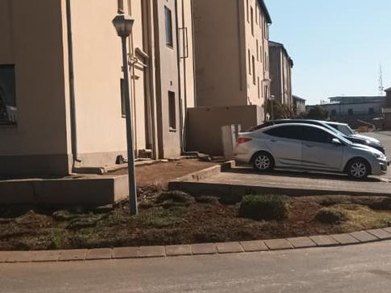 Exterior view of a multi-story townhouse complex showing the building facade, paved driveway, and surrounding grounds.