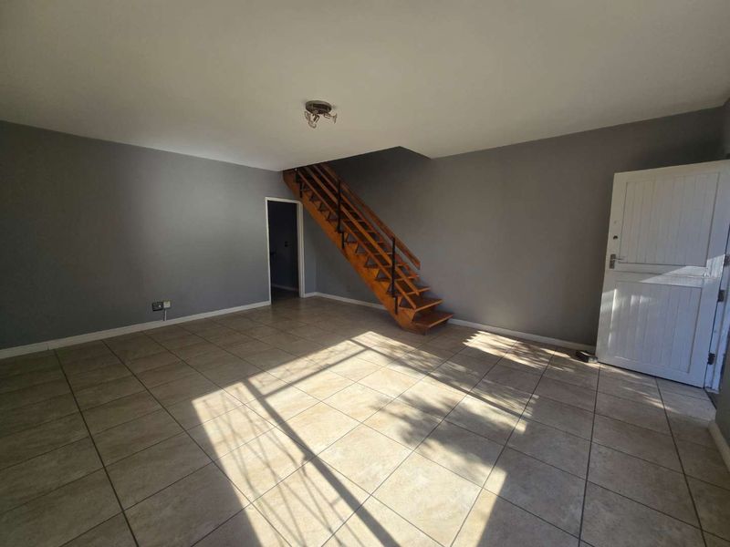 An open-plan living area featuring tiled flooring, a wooden staircase, and neutral grey walls, offering a blank canvas for interior design.