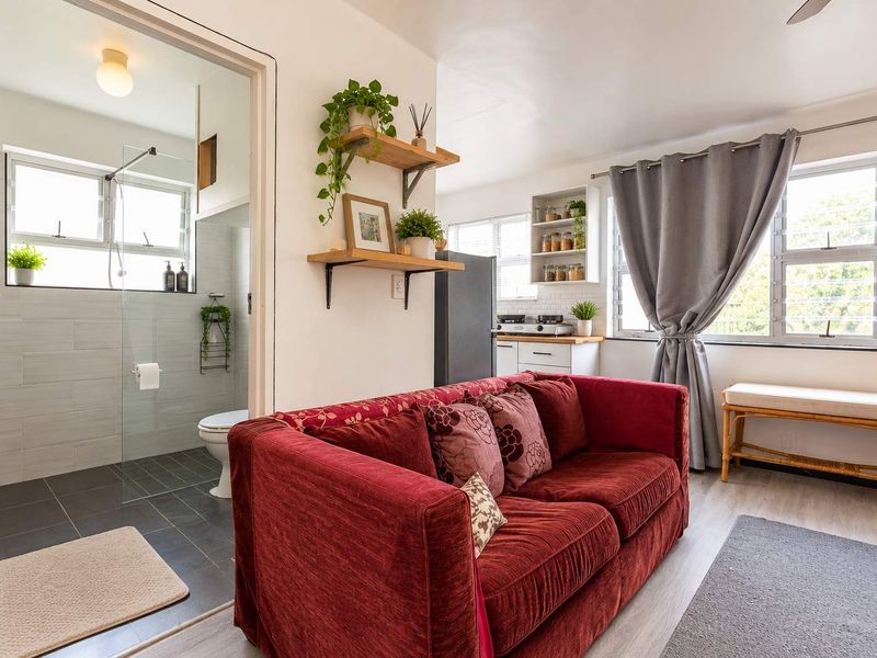 An open-plan living area featuring modern laminate flooring, a compact kitchen space, and an adjacent bathroom with a contemporary glass-enclosed shower.