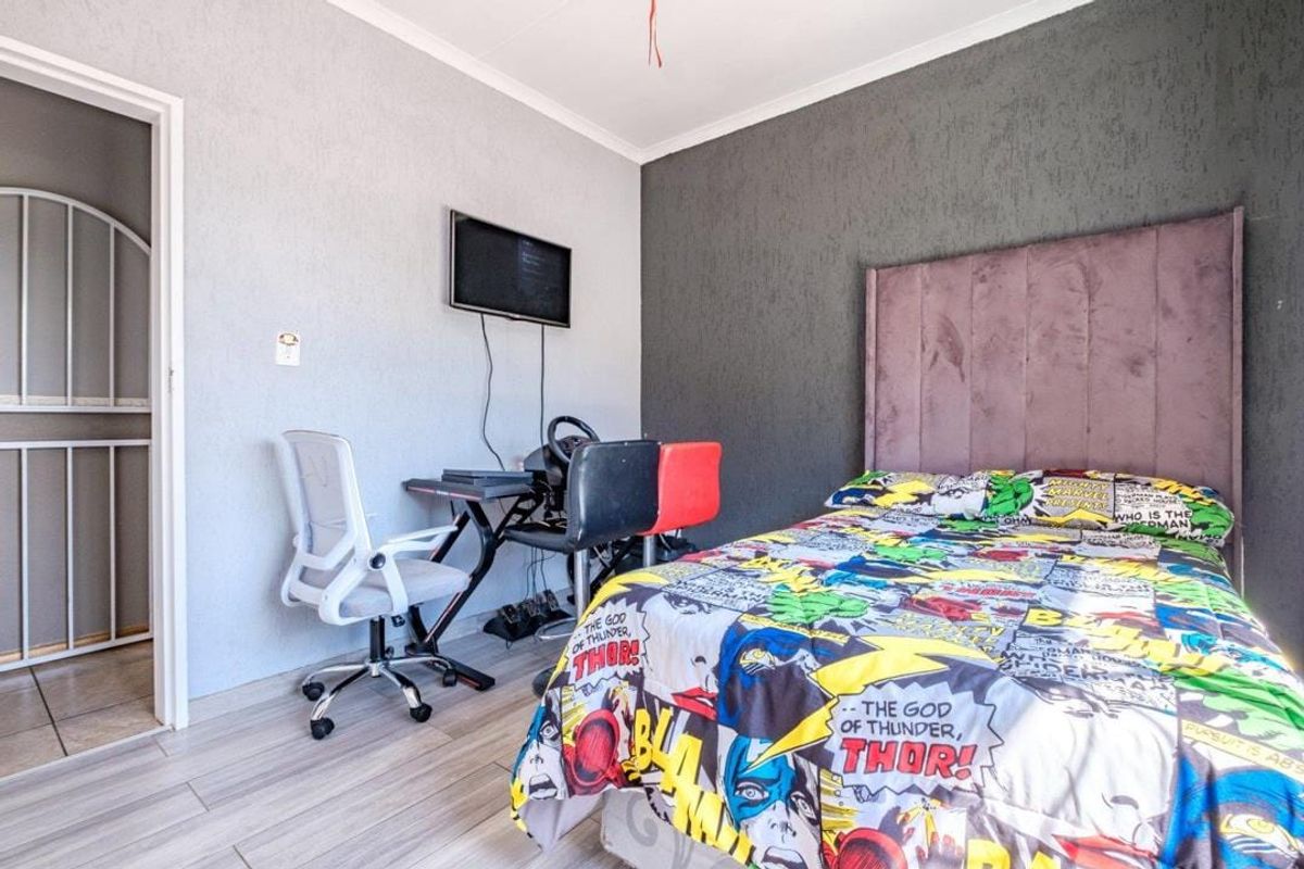 A bedroom featuring light-toned laminate flooring, a textured accent wall, and a built-in cupboard area.