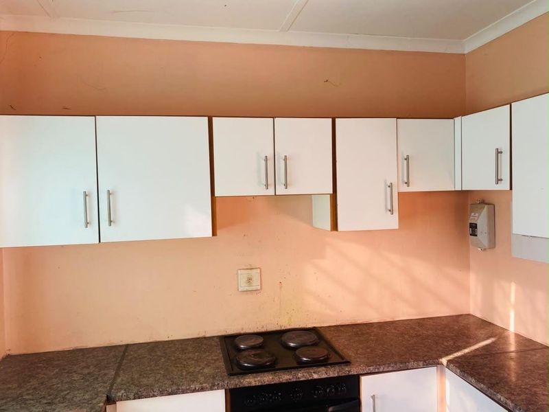 A functional kitchen area featuring white cabinetry, a dark laminate countertop, and a built-in electric hob and oven.