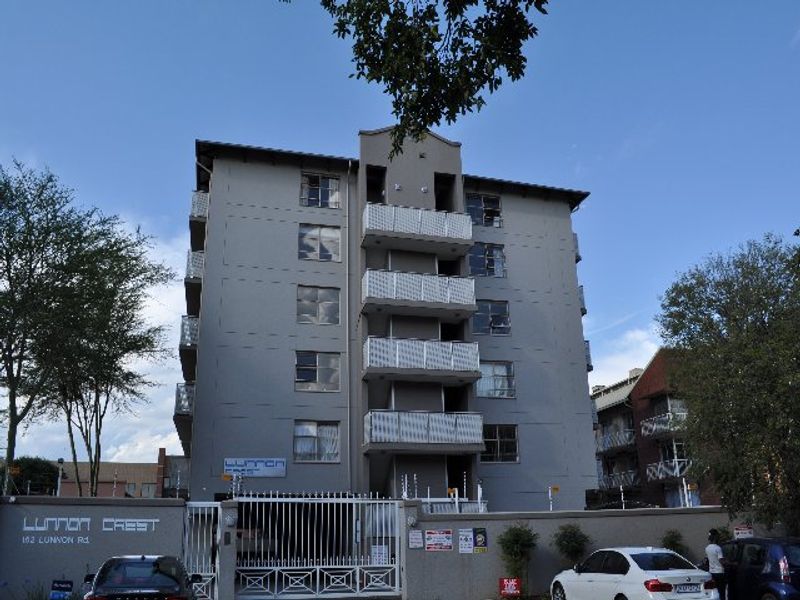 Front elevation of Lunnon Crest apartment complex featuring a multi-story building with balconies, secure perimeter wall, and gated entrance.