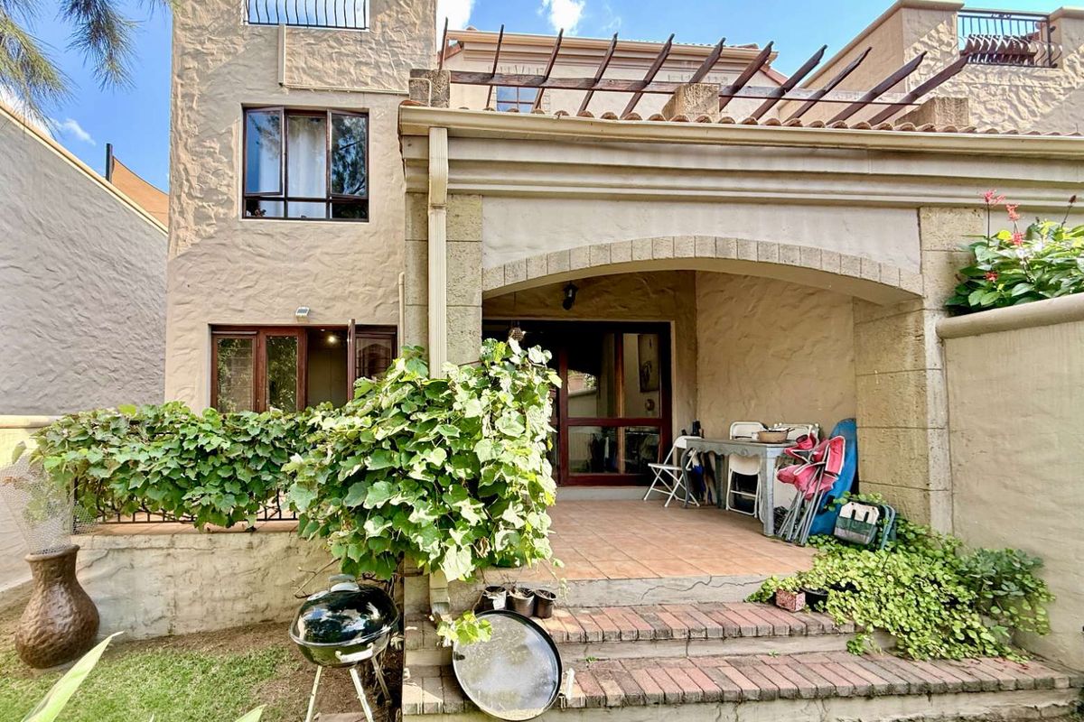Rear view of the apartment featuring a covered patio with arched detailing, brick steps, and a small garden area.