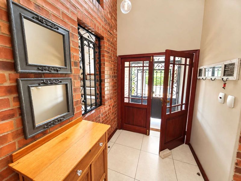 Welcoming entrance hall featuring exposed brick walls, ceramic floor tiles, and a secure timber-framed glass door with decorative wrought iron detailing.