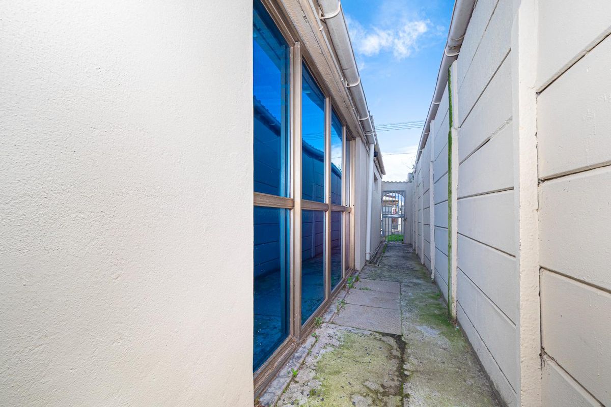A narrow side passage or exterior walkway featuring concrete paving, boundary walls, and large sliding glass doors.