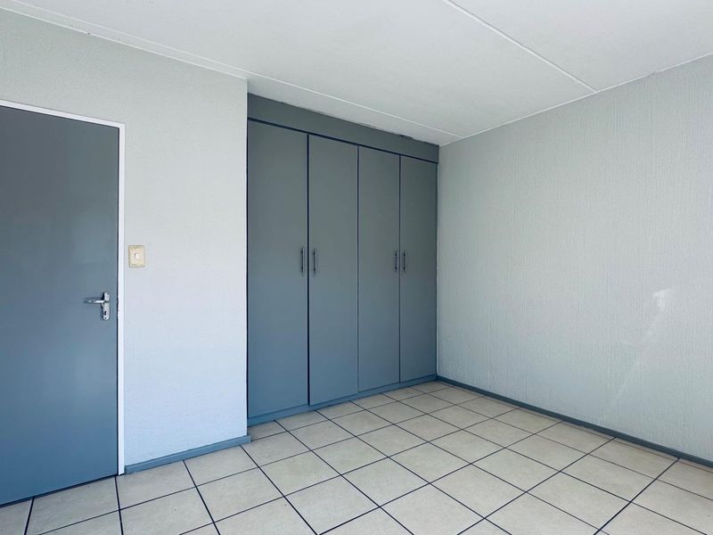A clean, empty bedroom featuring neutral tiled flooring and ample built-in cupboard storage with a modern grey finish.