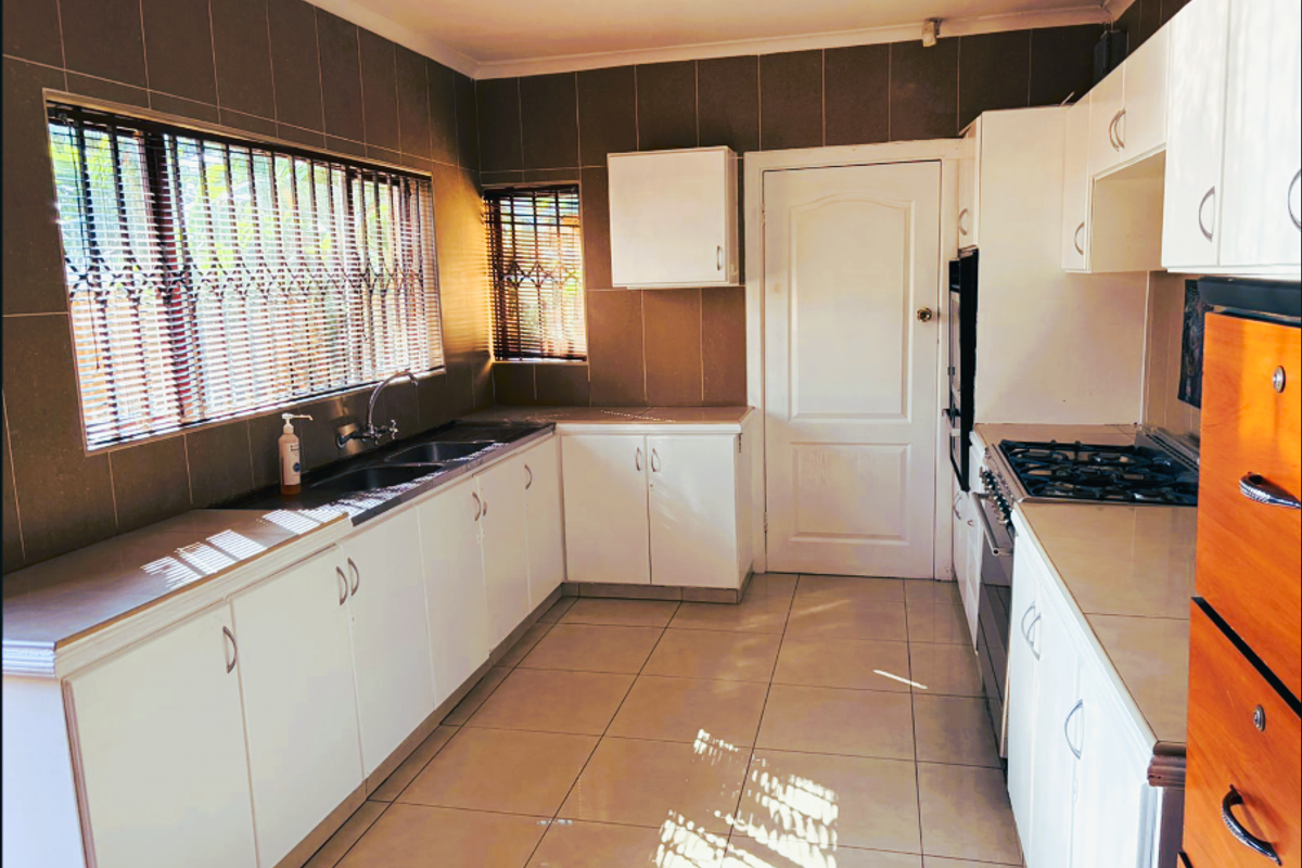 A functional kitchen featuring white cabinetry, tiled walls, a built-in oven, and a gas hob, offering a practical workspace for office staff.